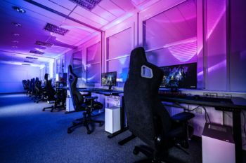 一间空房间，里面摆满了电脑和游戏椅。房间用蓝色和粉色照明，营造出一种情绪效果。